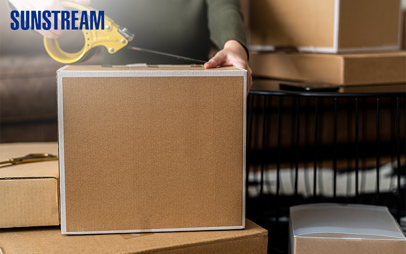 Person using a tape dispenser to seal a brown shipping box.
